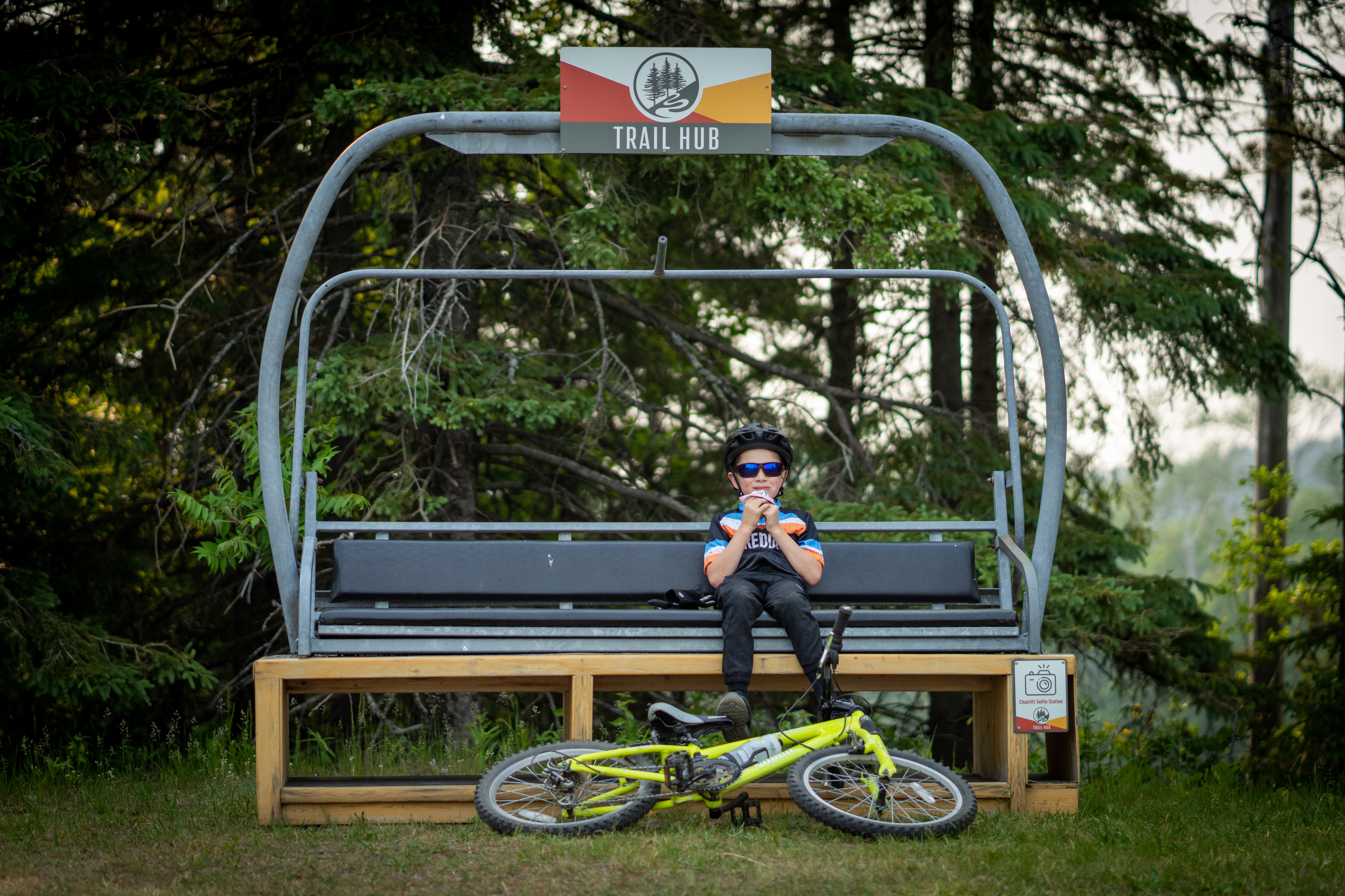 Kid sitting on a chairlift with his bike at his feet